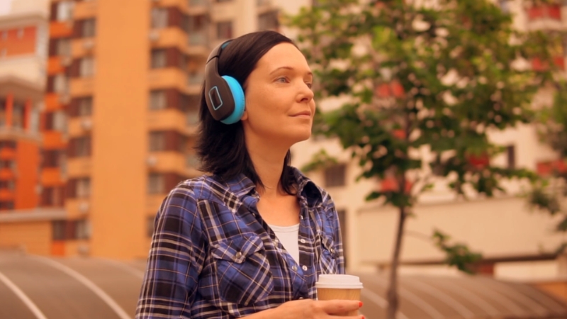 Woman wearing headphones outdoors holding a coffee cup and listening to an audiobook
