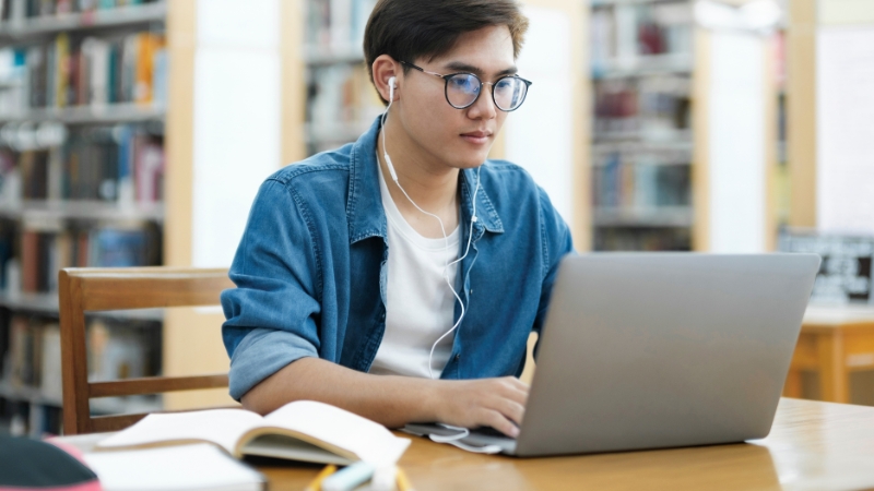 Man using a laptop in a library to track your reading beyond Goodreads and Notion