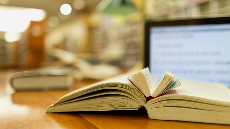 Open book on a desk in front of a laptop screen in a library, symbolizing how to track your reading